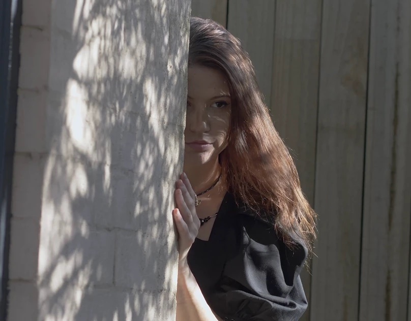 Woman half hidden behind a sunlit wall